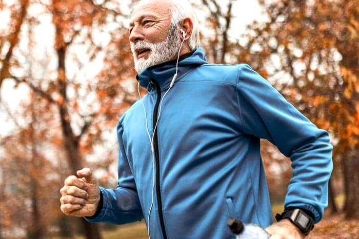 Senior man in fitness wear wearing headphones running in a park
