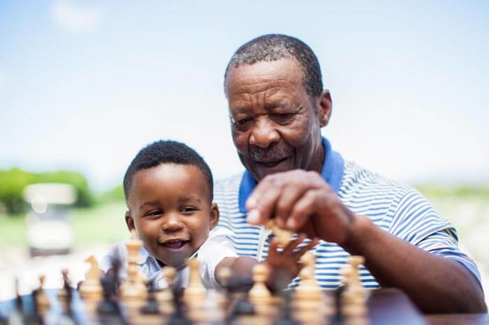 Older African grandfather playing chess with his grandson