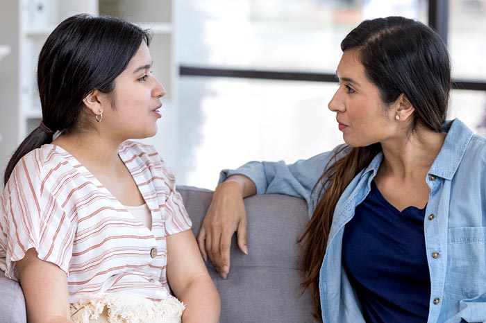 Mother and her teen daughter sitting on the couch talking