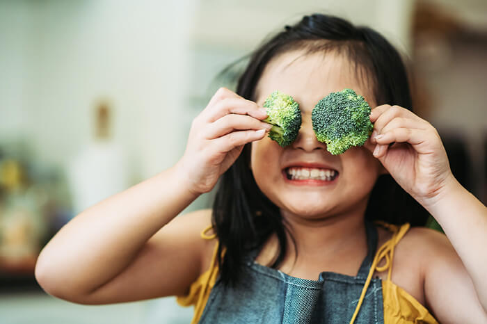 Cute silly kid holding broccoli in front of face
