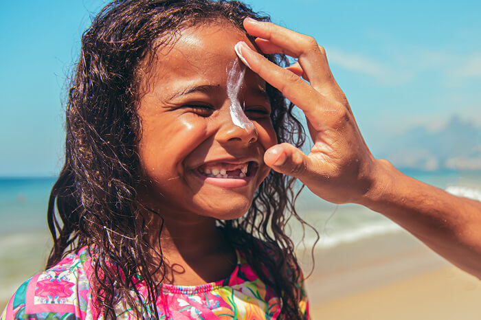 Little girl applying sunblock at the beach