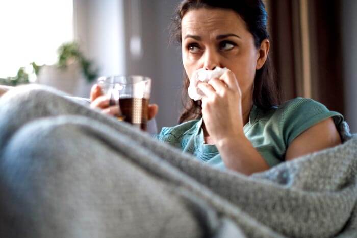 Sick woman lying in bed and blowing nose