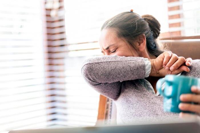 Woman coughs into elbow working form home