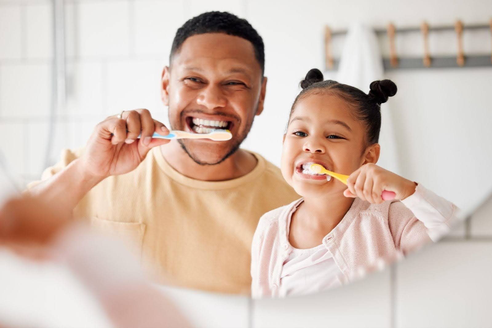 Dad and young daughter happily brushing teeth together